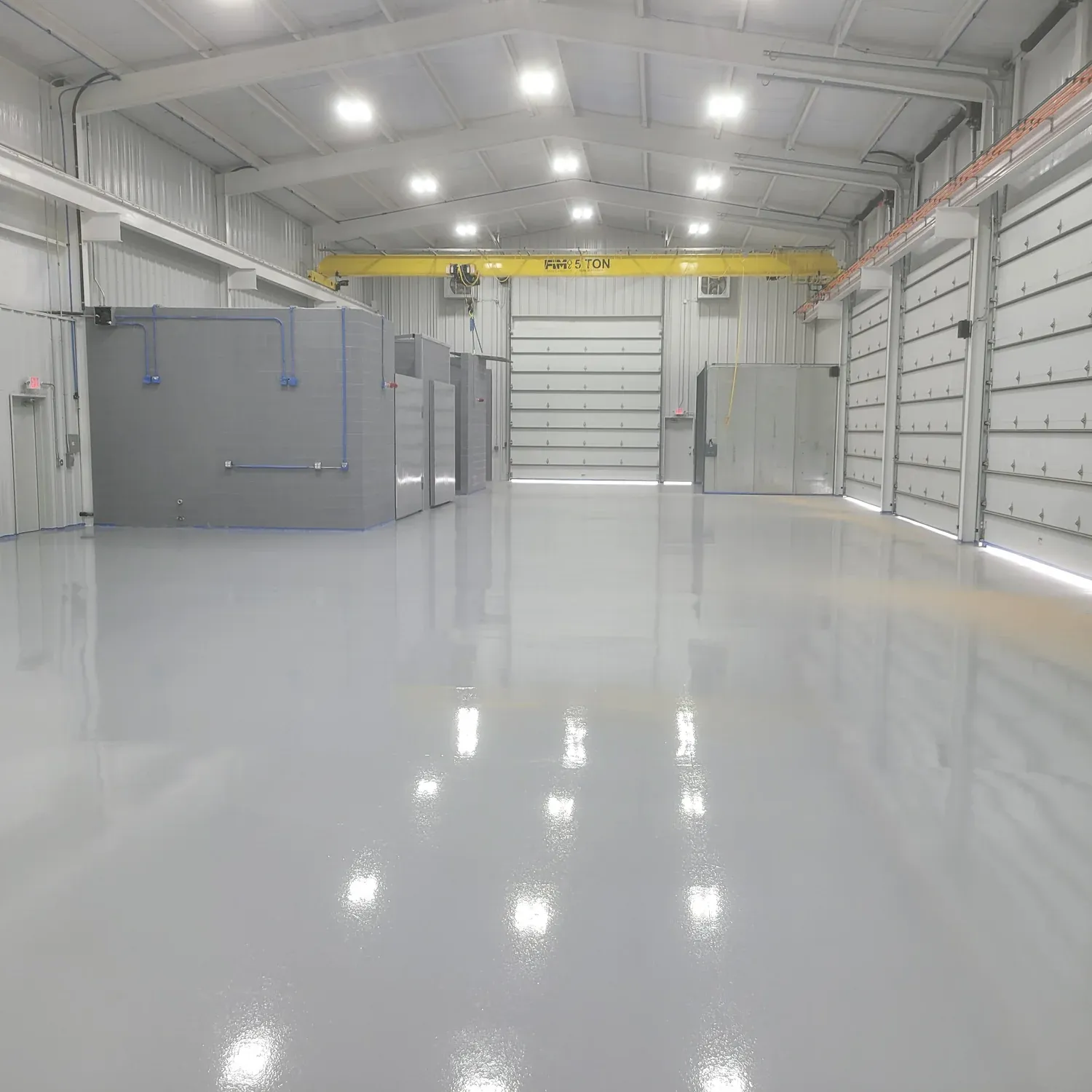 Bright, spacious industrial warehouse interior with polished concrete floors, high ceilings, overhead lights, yellow crane, and gray walls, conveying cleanliness.