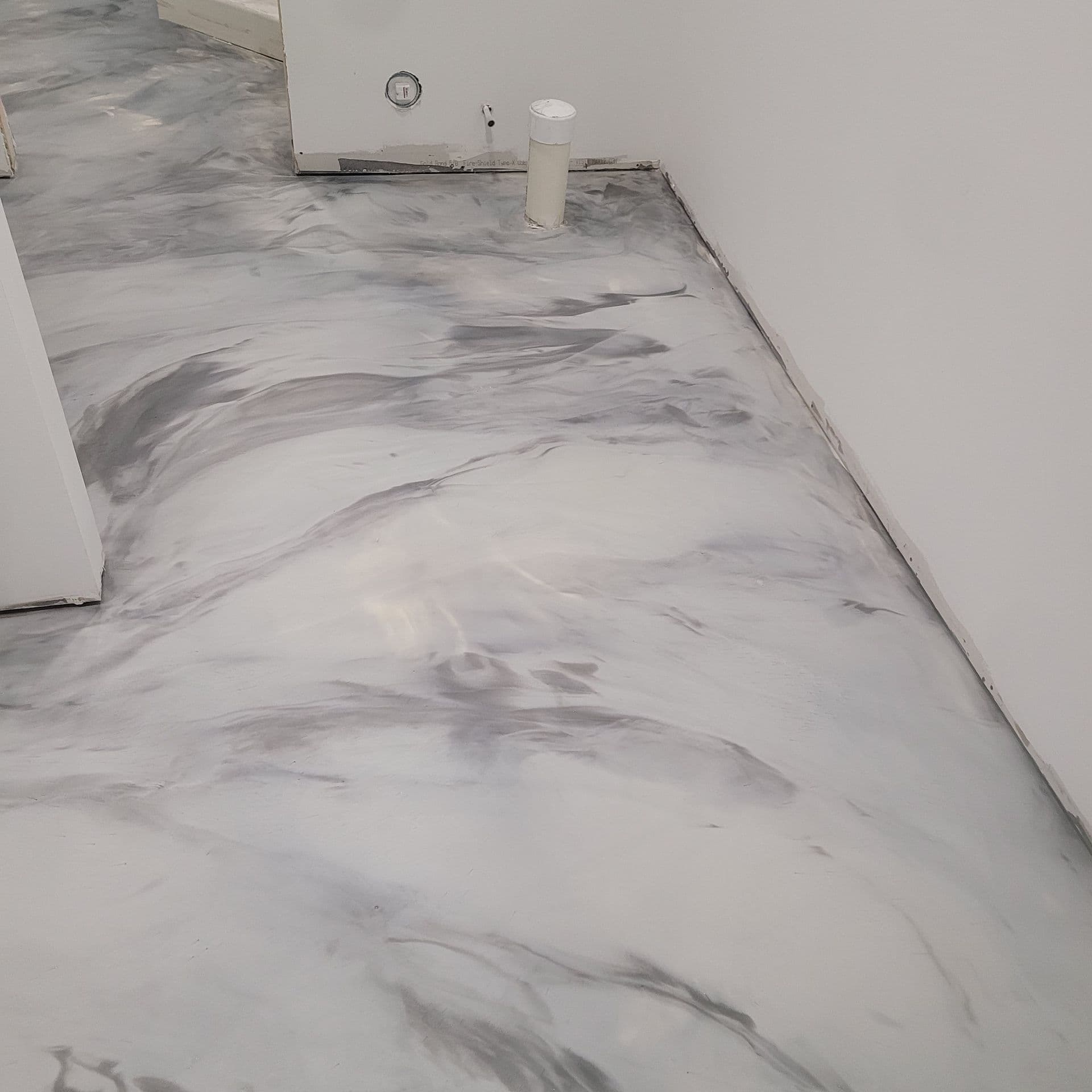 A room with unfinished white walls and a smooth, marbled gray and white epoxy floor, creating a modern, sleek, and minimalist look.