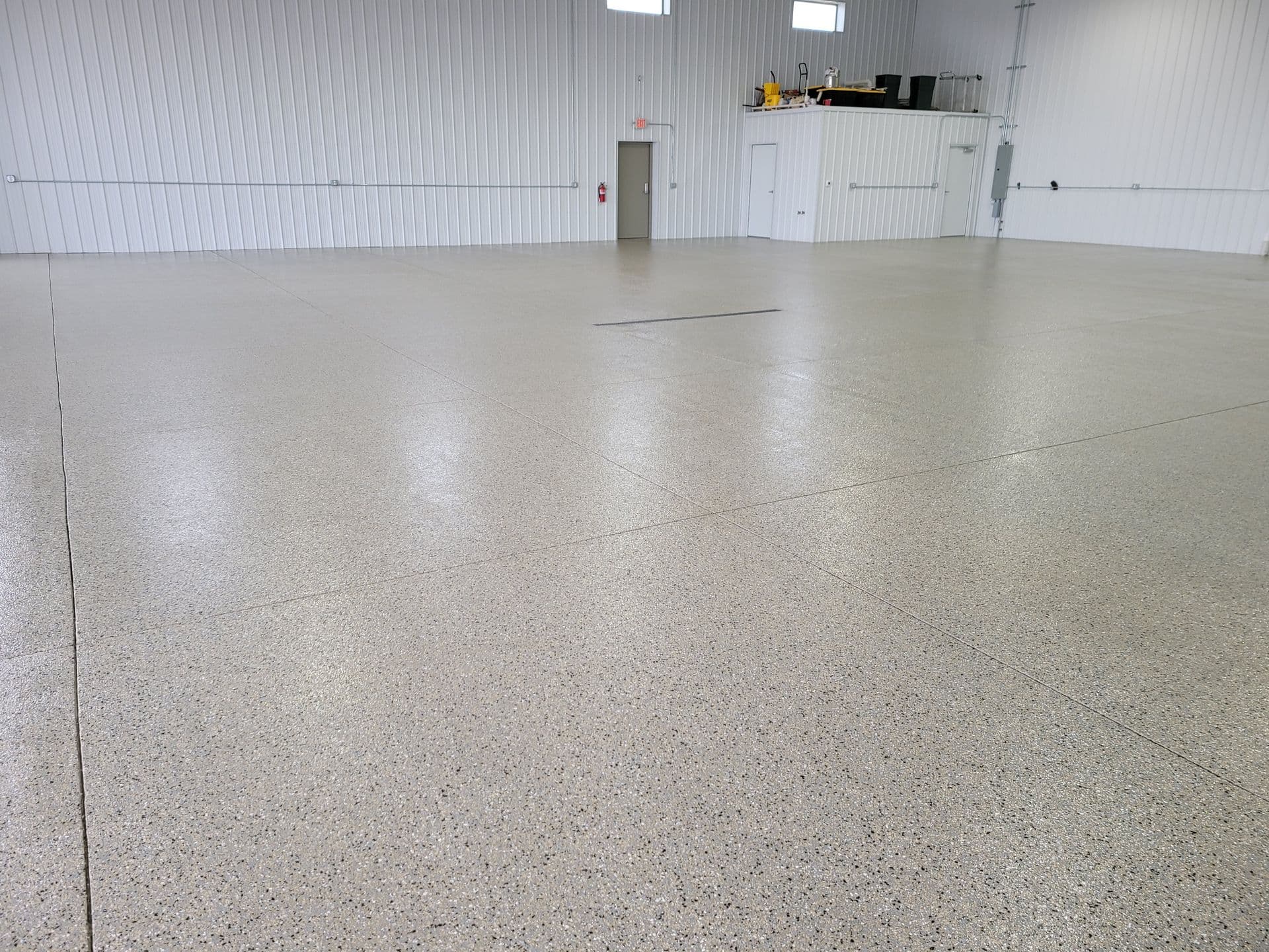 A large, empty warehouse with a polished concrete floor. The walls are white with subtle vertical lines, and there are small, elevated windows.
