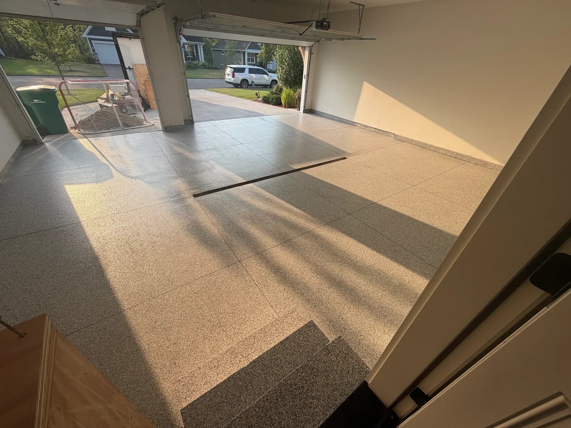 Spacious empty garage interior with polished concrete flooring, open garage door revealing driveway and residential street with parked white vehicle