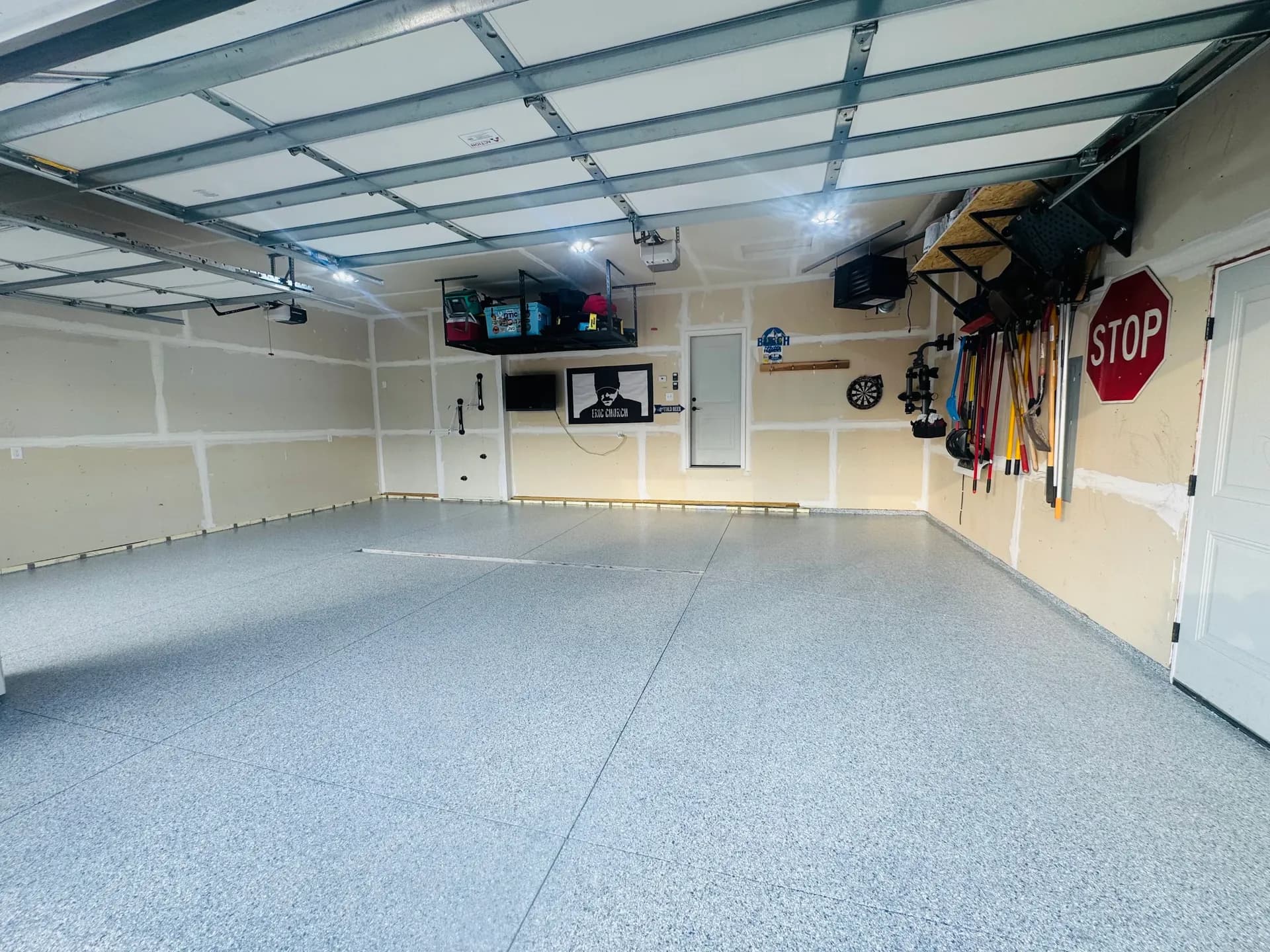 Well-organized garage interior with epoxy flooring, metal ceiling framework, wall-mounted tool storage, stop sign, and shelving with equipment and supplies