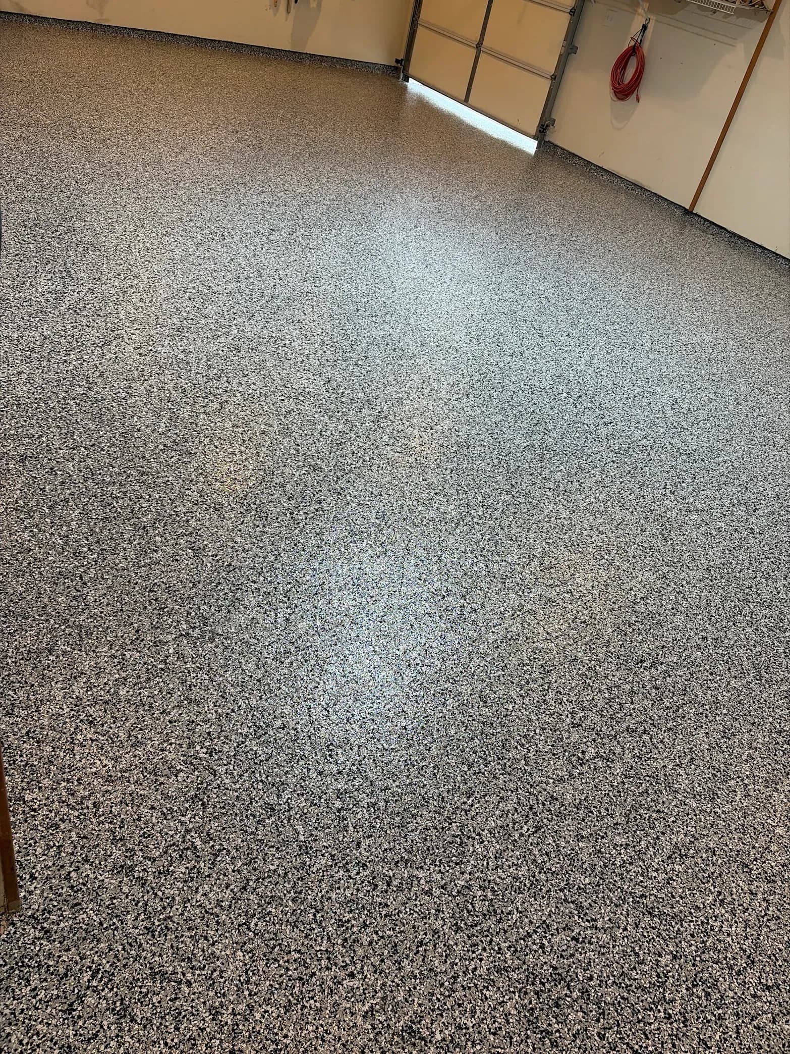 Speckled gray epoxy garage floor with light stripe down center, garage door and red coiled rope visible along wall