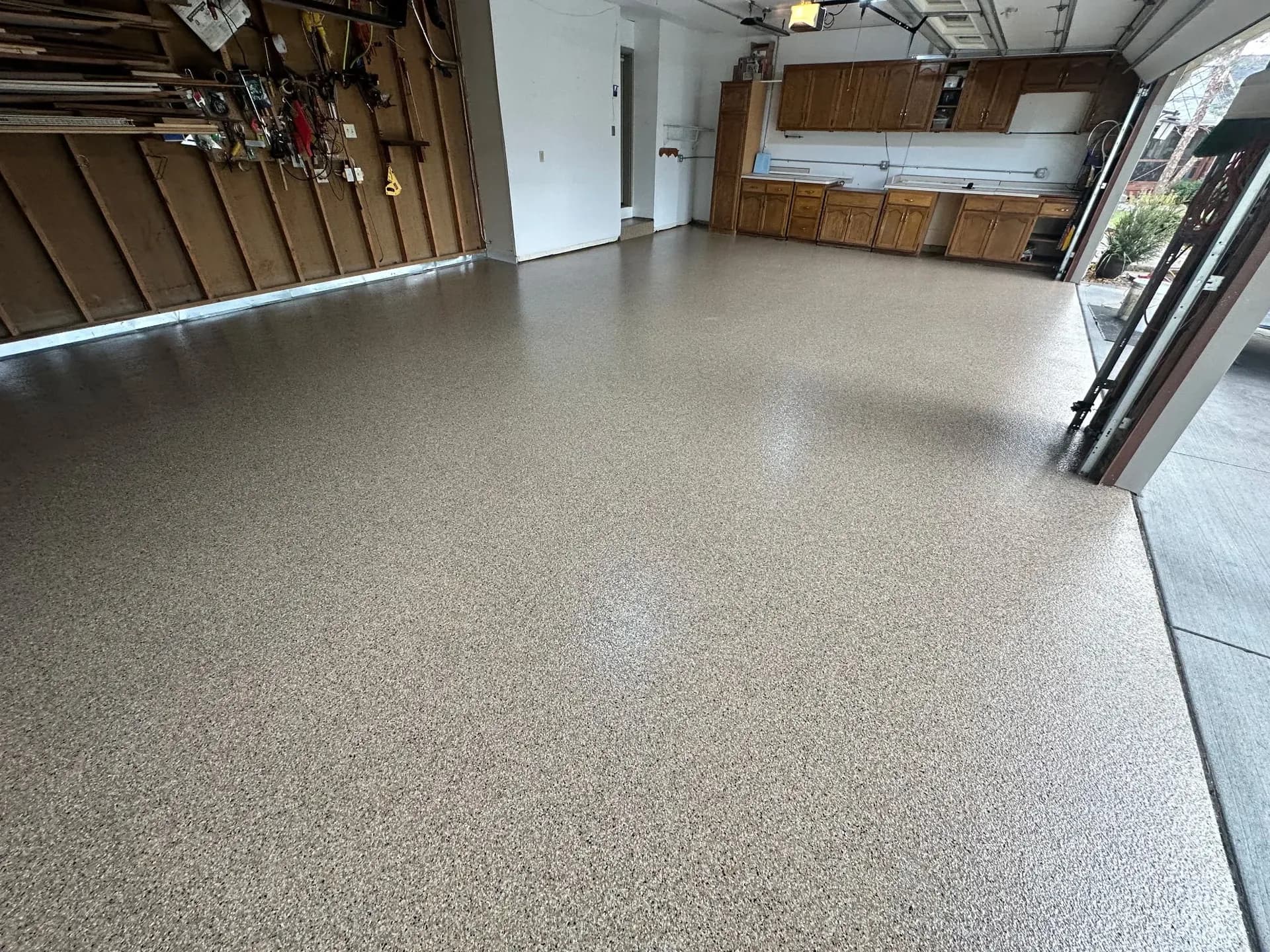 Spacious garage interior with sealed concrete floor, wooden cabinetry along walls, and open garage door with driveway visible outside