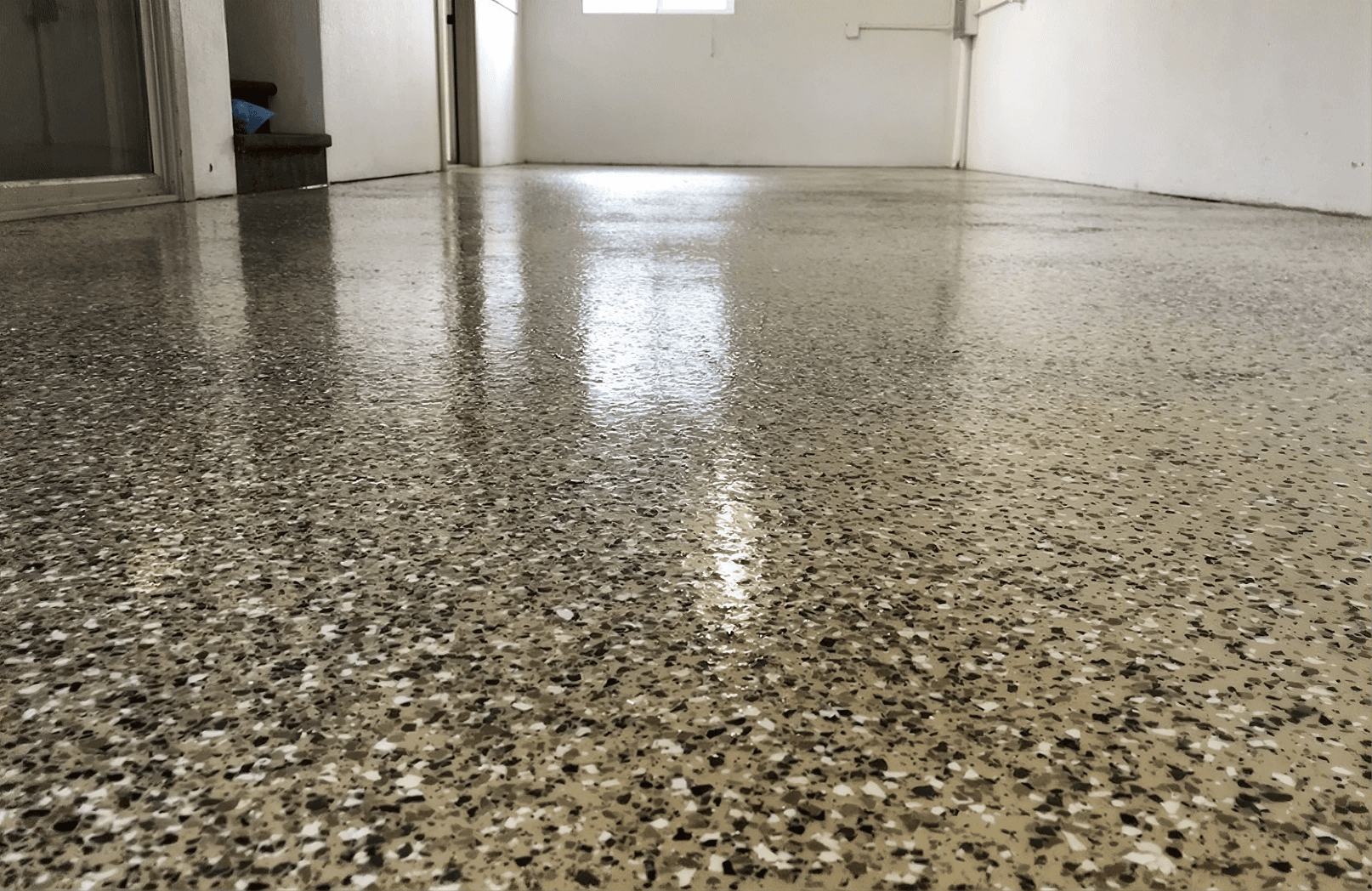 Shiny, polished epoxy floor in an empty room with white walls and a small window at the far end, creating a clean and spacious atmosphere.